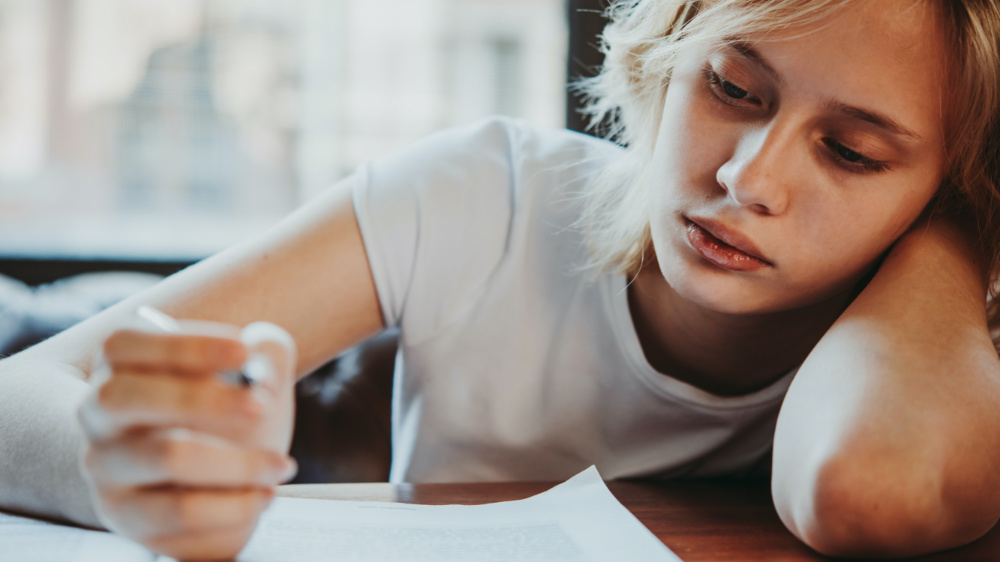 adolescente en train d'écrire avec le coude sur son banc